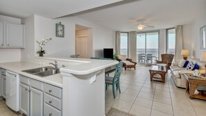 A modern kitchen with a central island, dining area with chairs, a sofa, and a balcony with a view.