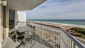 A balcony with a table and chairs overlooking a beach.