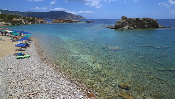 A beach with clear water, rocky shore, and umbrellas. - Cavo Marelia (Karpathos)