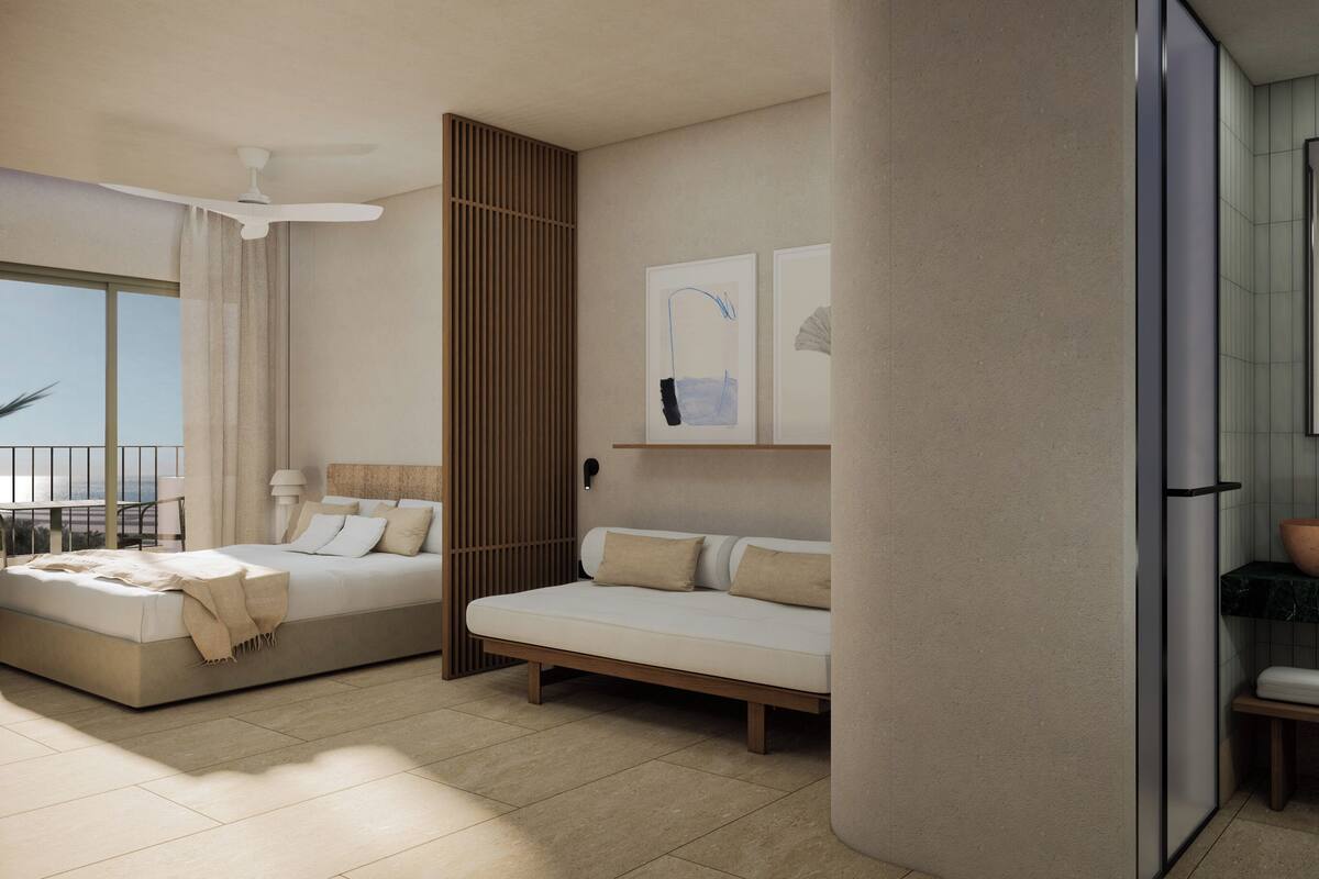 Una habitación de hotel moderna con una cama grande, un sofá, un balcón con vistas y un baño con lavamanos y espejo amplios.
