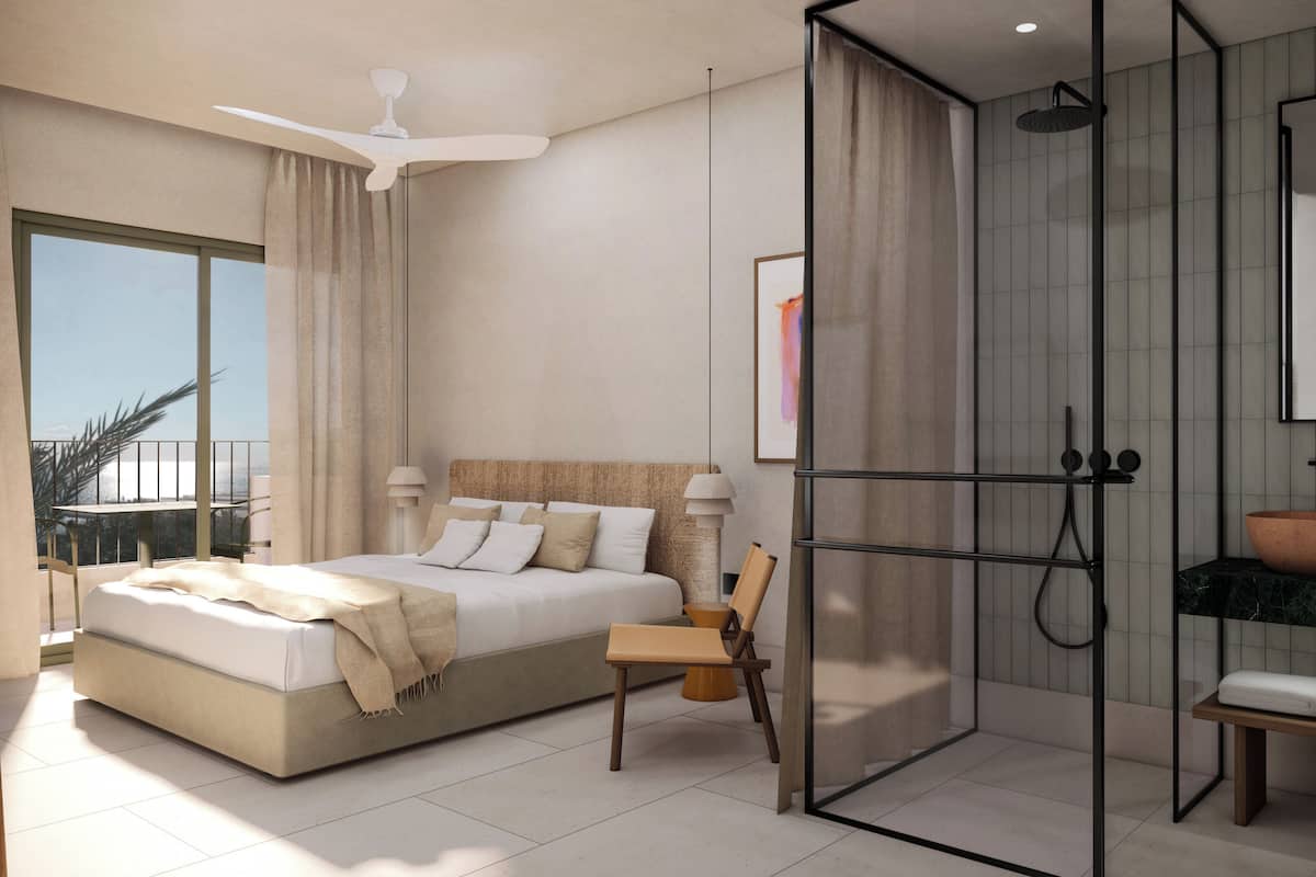 Un dormitorio moderno con una cama grande, una silla, zona de ducha con cabina de cristal y un baño con lavabo grande y espejo.