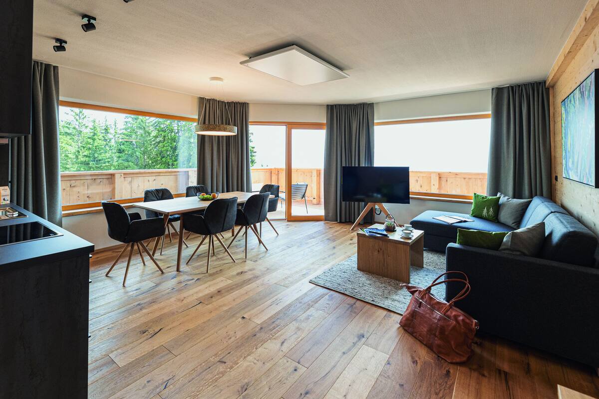 Ein modernes Wohnzimmer mit Essbereich, Fernseher und einem Balkon mit Blick auf Bäume.