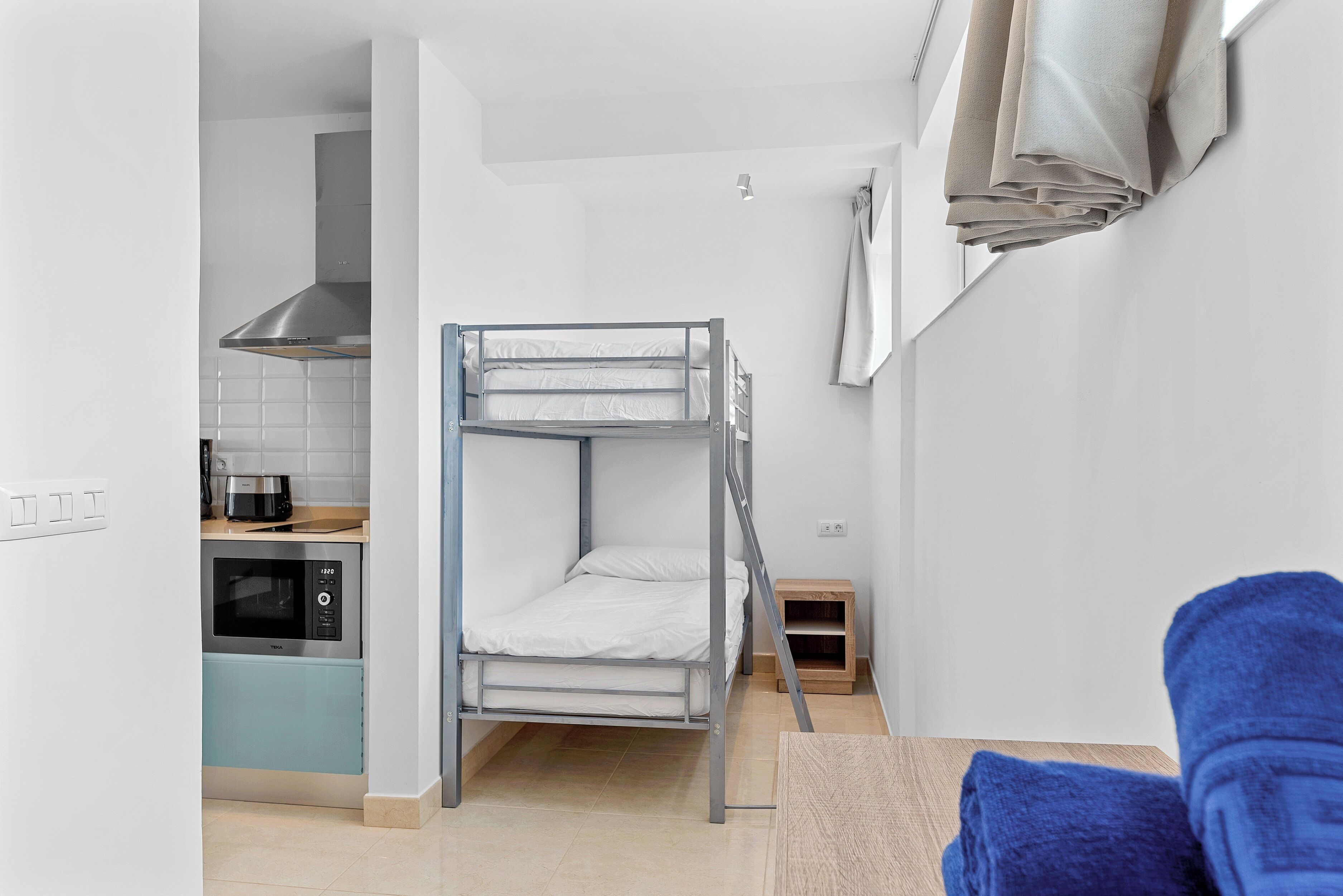 Una stanza compatta con un letto a castello, angolo cottura con forno a microonde e un piccolo tavolo di legno.