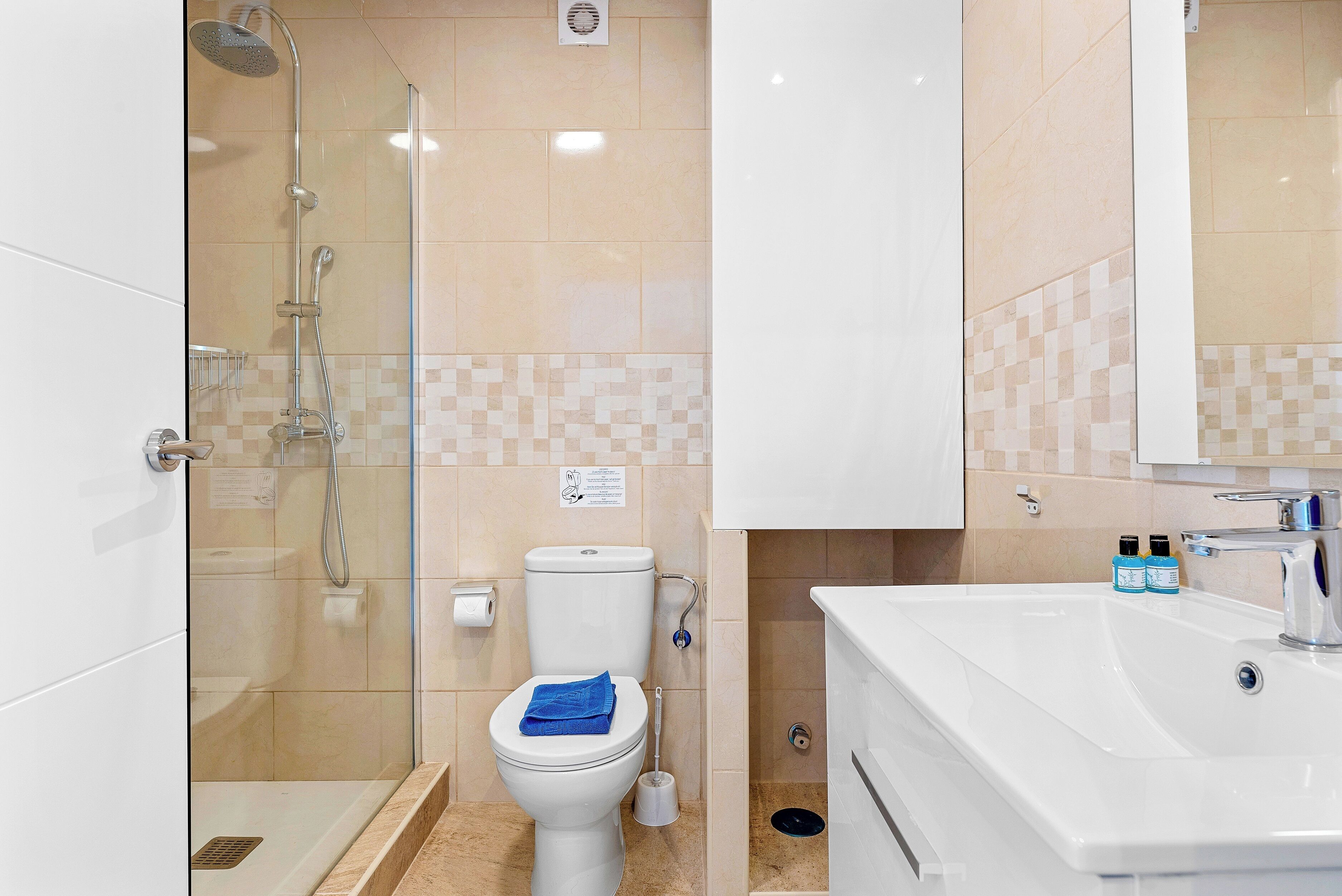 Un baño moderno con ducha de vidrio, inodoro blanco y lavamanos blanco con espejo arriba.