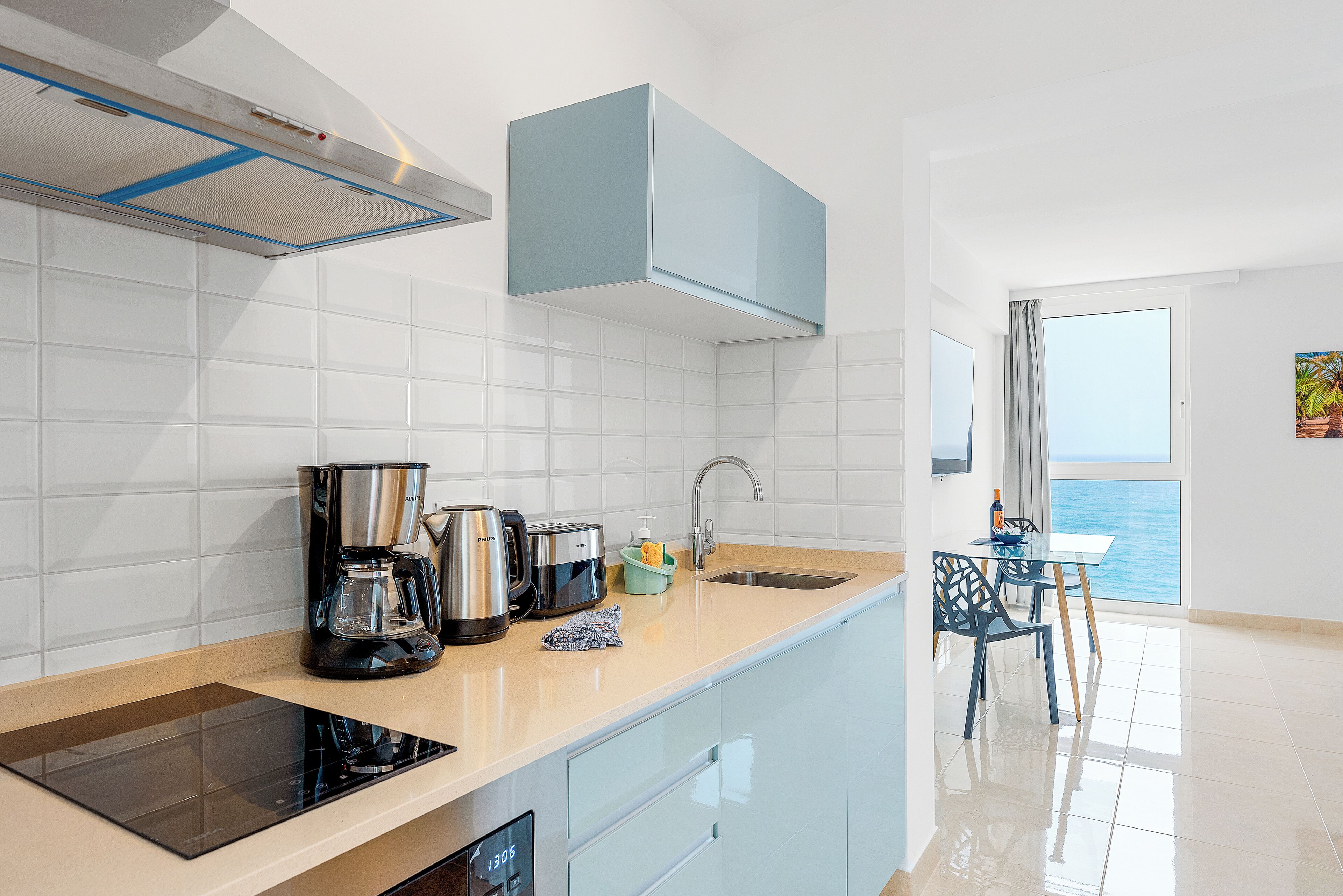 Una cocina moderna con estufa integrada, cafetera y vistas al mar a través del ventanal.