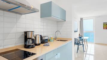 Una cocina moderna con estufa integrada, cafetera y vistas al mar a través del ventanal.