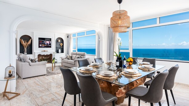 A modern dining area with a glass table, dark chairs, and a view of the ocean. - Ocean Vistas 24 (Puerto de la Cruz)