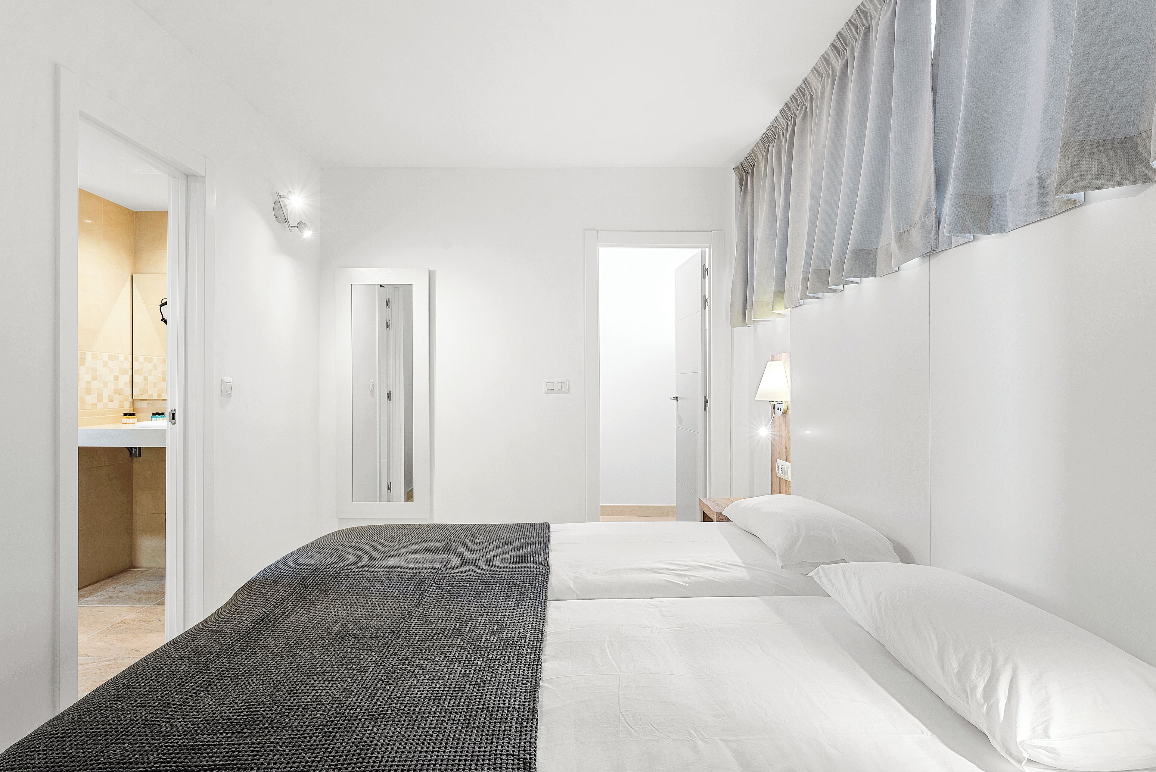 Habitación de hotel con una cama, una mesita de noche con lámpara y un baño visible a través de una puerta abierta.