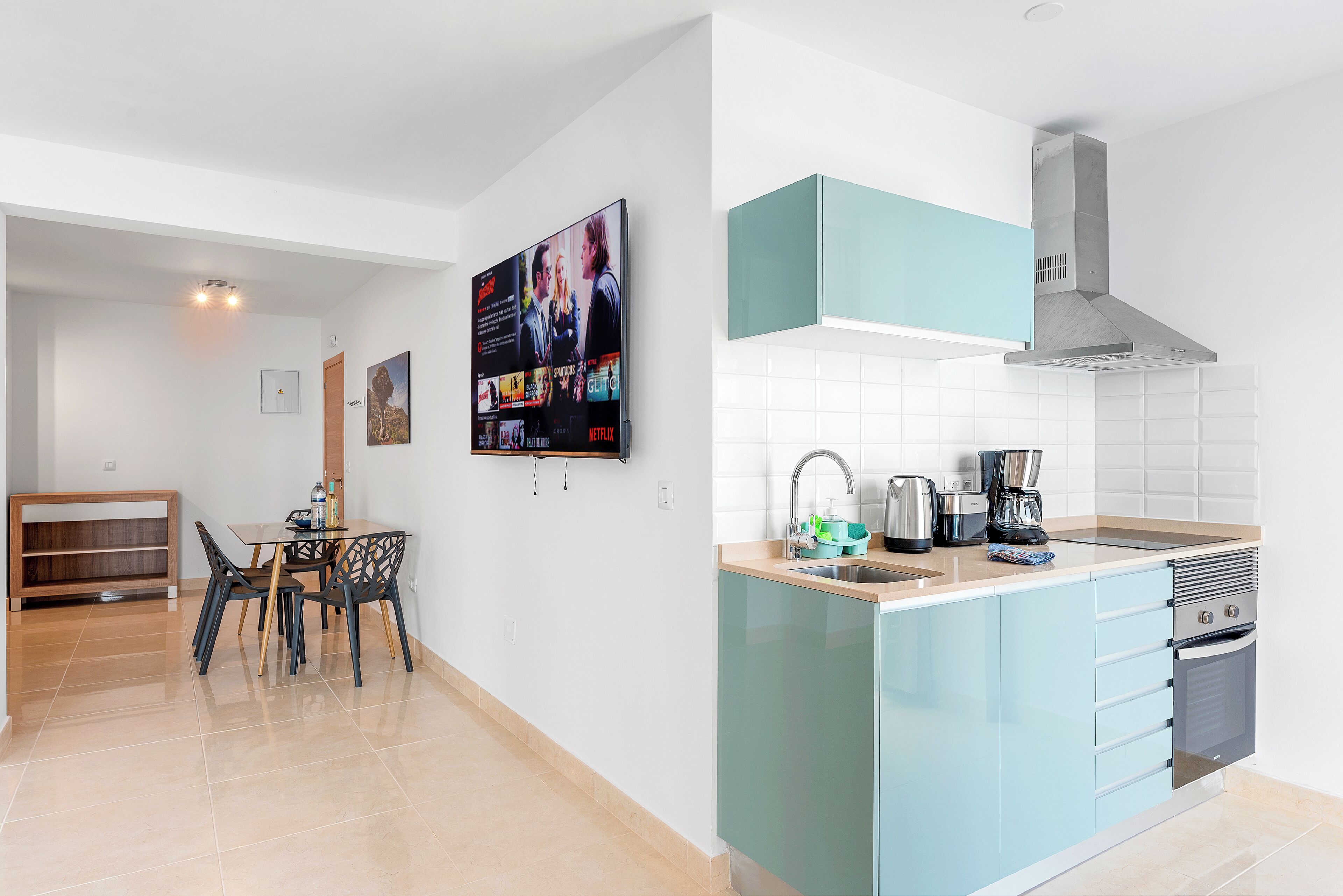 A modern kitchen with a built-in island, a dining area with a table and chairs, and a flat-screen TV mounted on the wall.