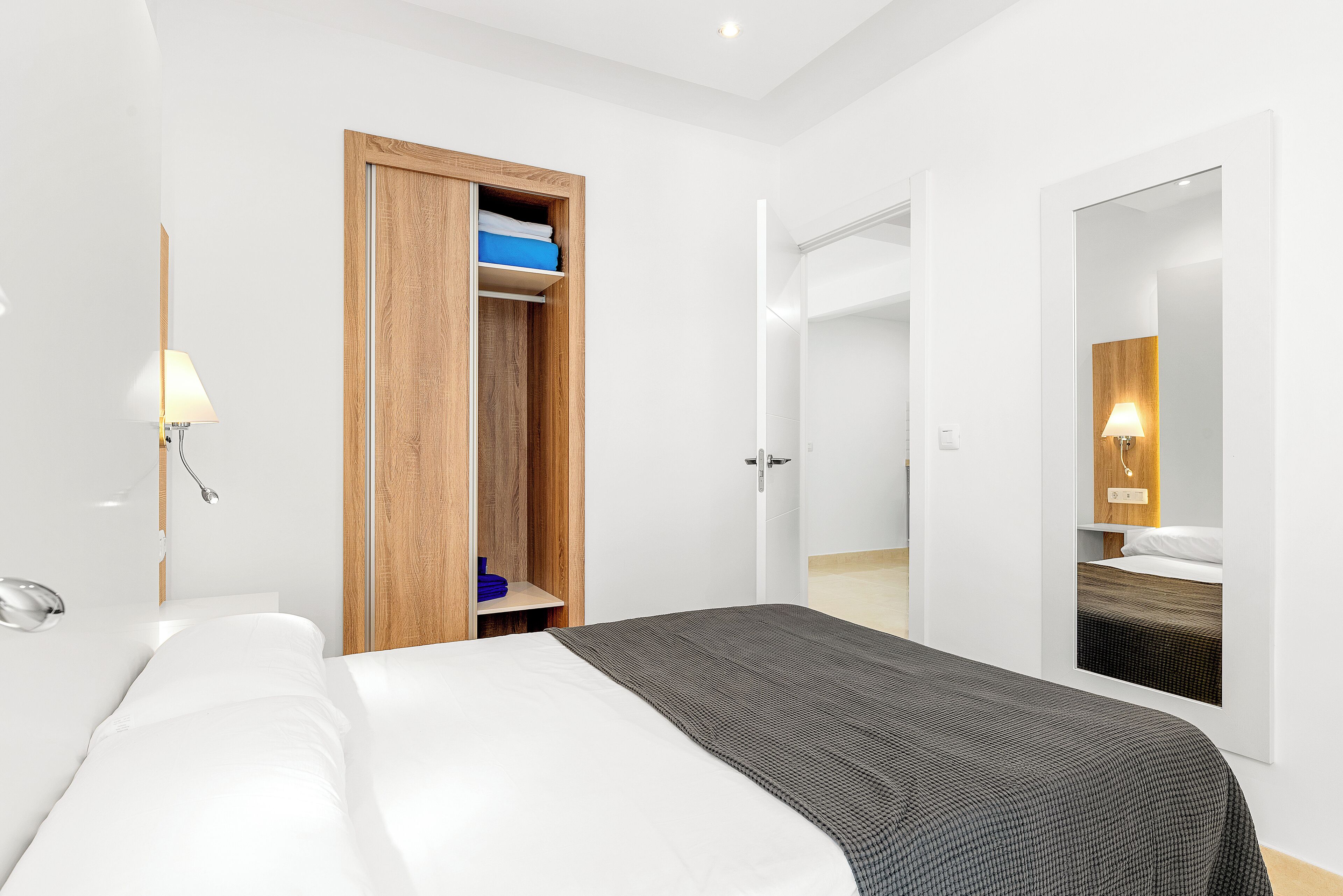 Una habitación de hotel moderna con una cama grande, un armario de madera, un espejo y un baño con ducha.
