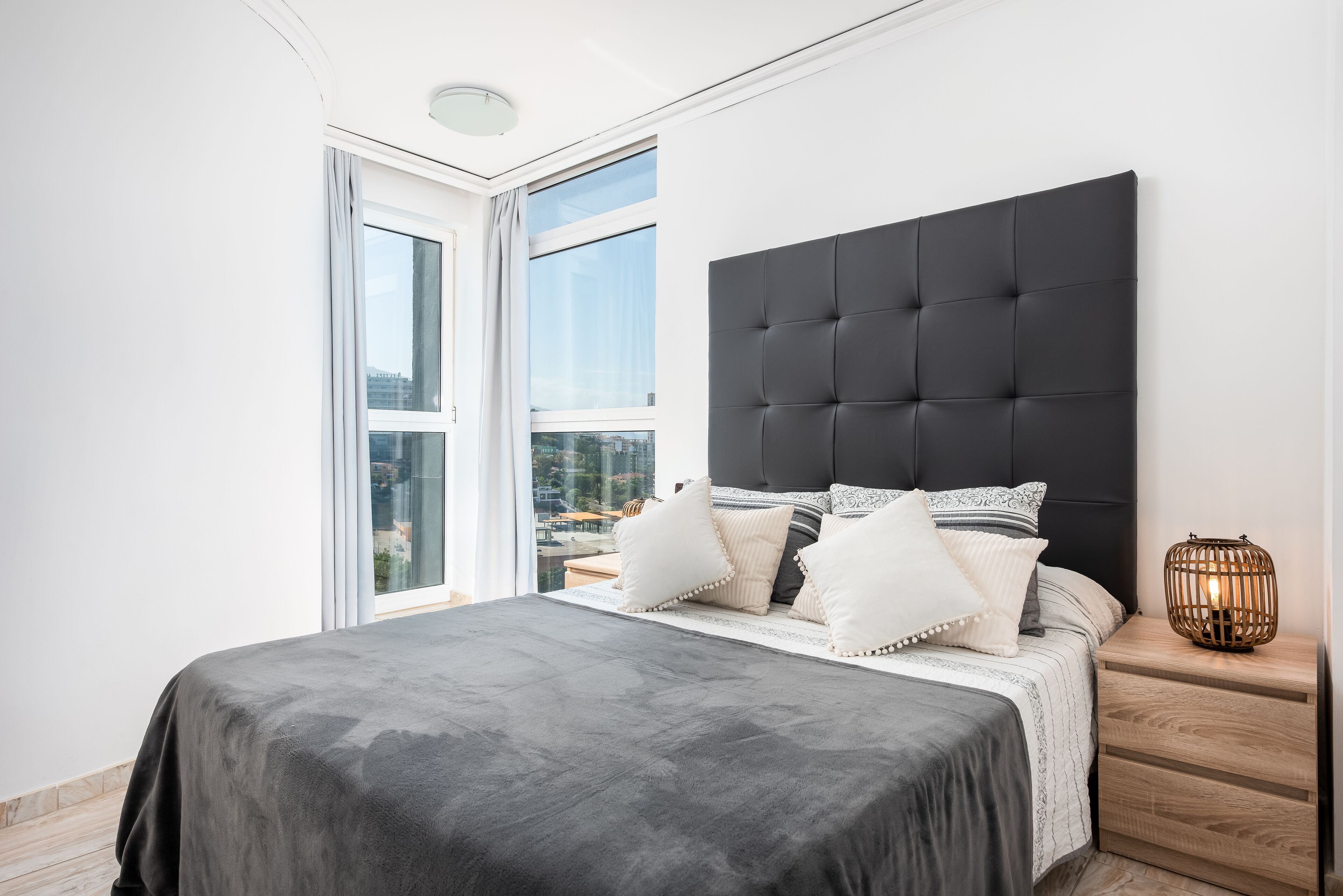A modern bedroom with a large bed, a dark headboard, and a nightstand with a lamp.