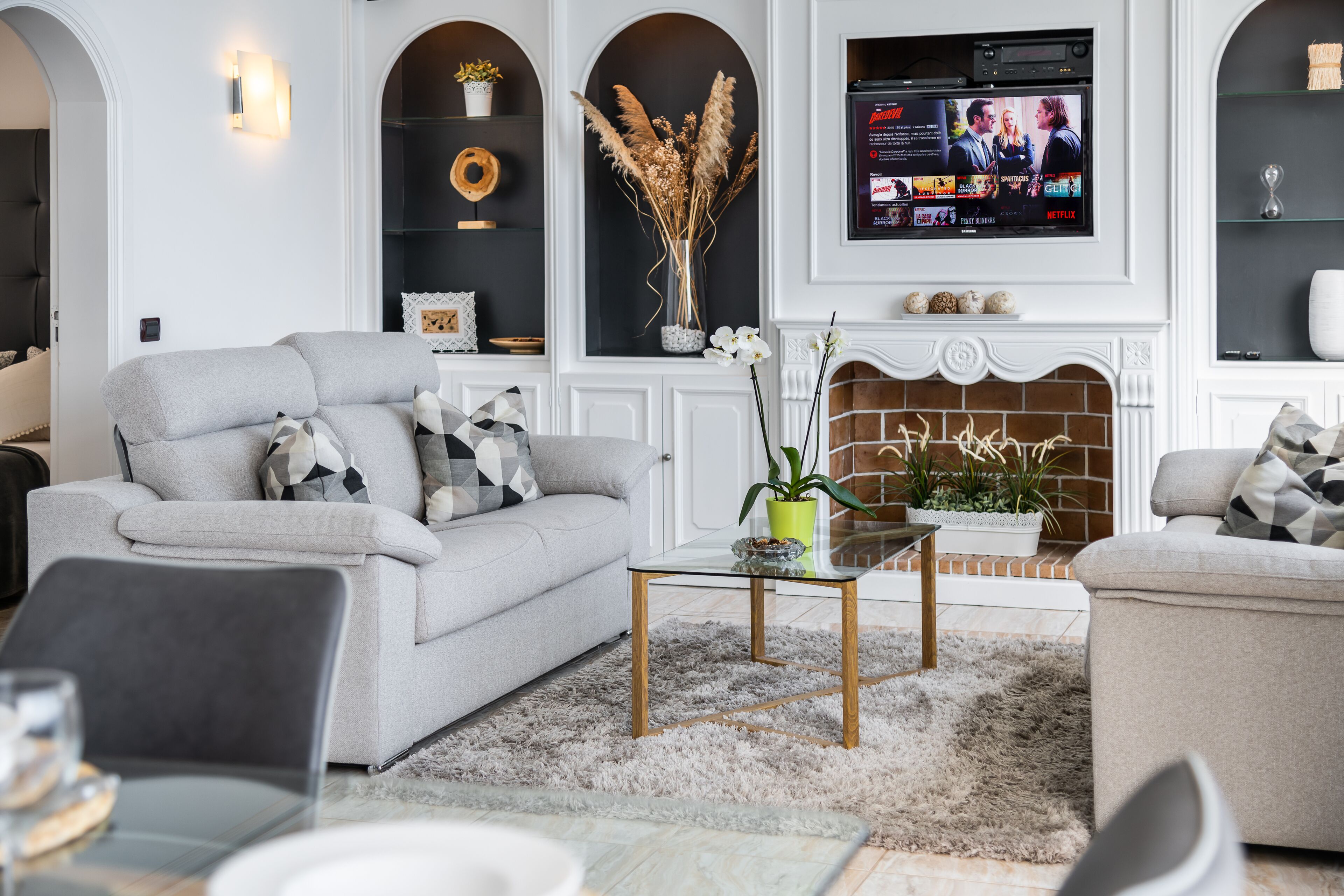 Una sala de estar con un sofá gris, una mesa de centro y un televisor de pantalla plana sobre la chimenea.