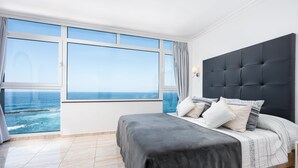 A bedroom with a large window, a bed with a dark headboard, and a view of the ocean. - Ocean Vistas 24 (Puerto de la Cruz)