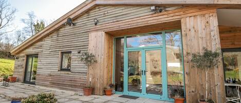 A wooden cabin with a large glass door and windows, surrounded by potted plants and a stone-paved entrance.