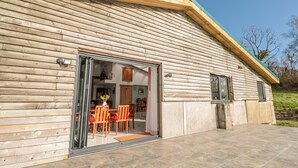 Un edificio de madera con un amplio escaparate de vidrio que da a un espacio con una mesa y sillas para comer.