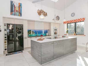A modern kitchen with a large island, a built-in oven, and a view of a coastal scene.