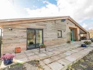 A wooden house with a stone-paved entrance, large sliding glass doors, and a covered porch area.