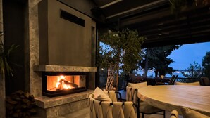 An outdoor patio area with a stone fireplace, comfortable seating, and a view of the evening sky. - Cunda Pier Otel (Ayvalik)
