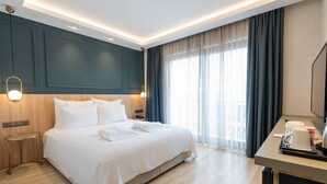 A hotel room with a large bed, bedside tables, a desk with a chair, and a large window with curtains. - Cunda Pier Otel (Ayvalik)