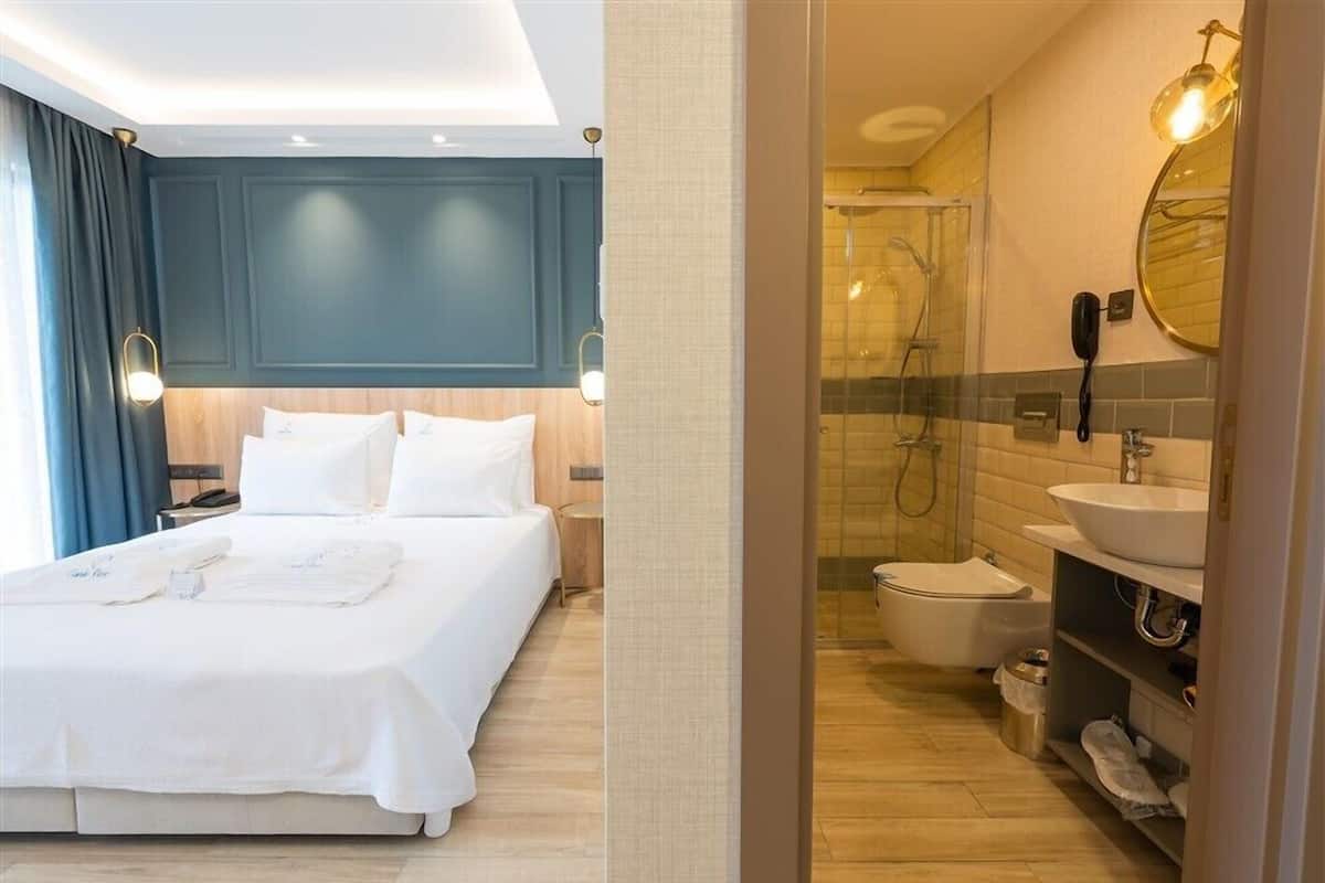 A hotel room with a bed, bedside table, and a bathroom with a shower, toilet, and sink.