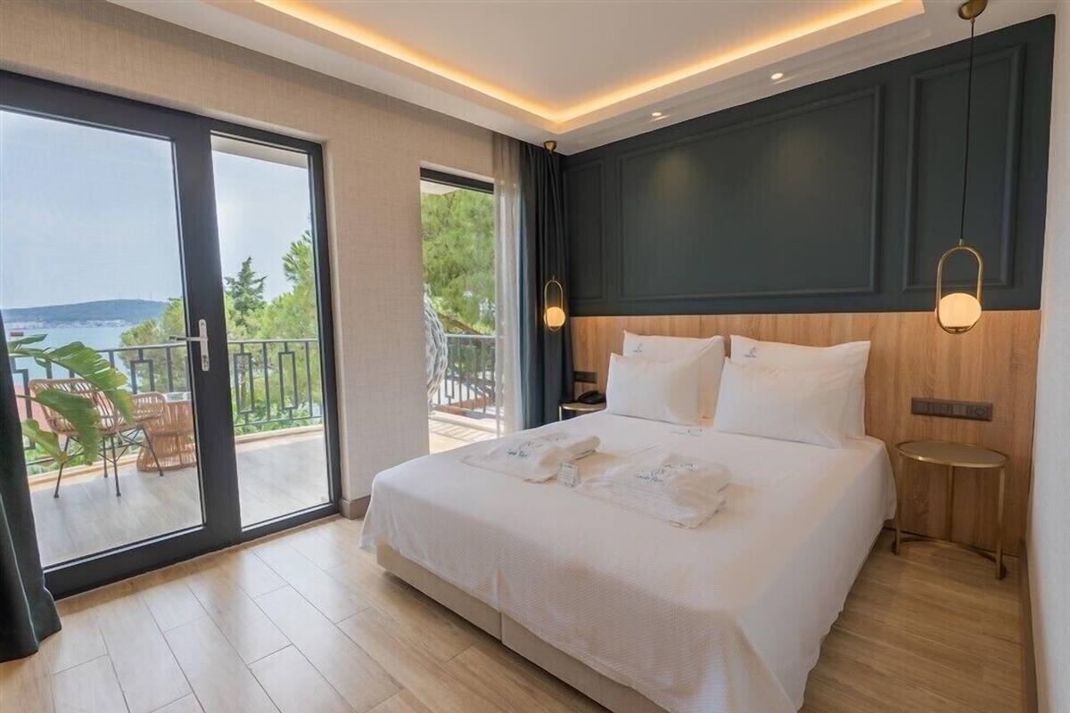 A hotel room with a large bed, a balcony with a view, and a wooden floor.