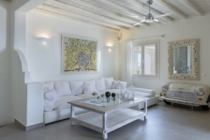 Ein helles Wohnzimmer mit einem weißen Sofa, einem Glastisch, einem Oldtimer und einem großen abstrakten Gemälde.