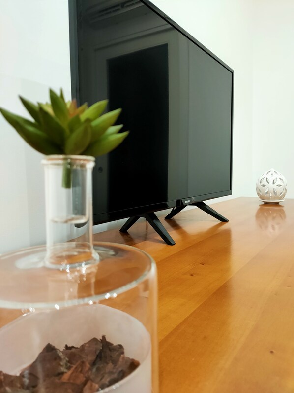 Een moderne woonkamer met een flatscreen televisie op een standaard, een glazen vaas met een vetplant en een decoratieve bol op een houten vloer.