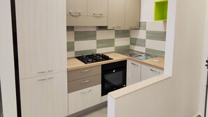 A modern kitchen with white cabinets, a gas stove, an oven, and a green shelf. - Central apartment in private area (Barletta)