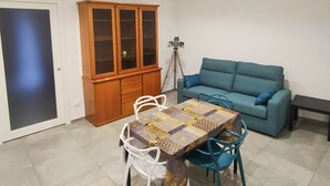 A living room with a blue sofa, a wooden cabinet, a dining table with chairs, and a tripod. - Central apartment in private area (Barletta)