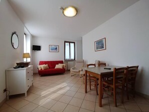 Una habitación amplia con un sofá rojo, una mesa de comedor con sillas, un armario blanco, un televisor y dos cuadros en las paredes.