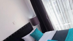 A neatly made bed with a black headboard, white and teal pillows, and a teal blanket. - Stay.Plus Royal Suburbs By Tsavo (Nairobi)