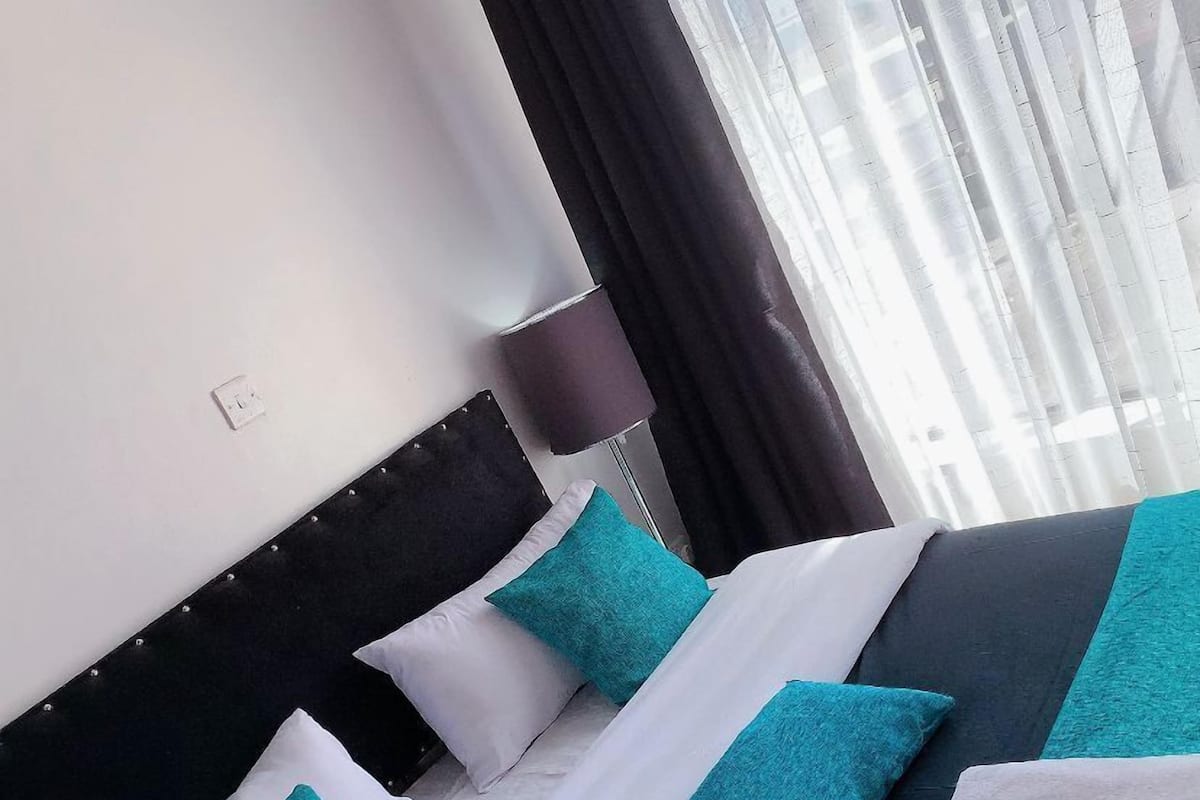 A neatly made bed with a black headboard, white and teal pillows, and a teal blanket.