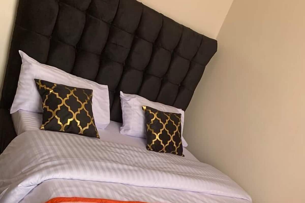 A bed with a tufted headboard, white bedding, and two decorative pillows with a black and gold pattern.