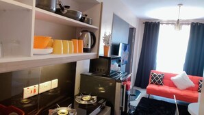 A compact living space with a kitchenette, a sofa, and a television. - Stay.Plus Royal Suburbs By Tsavo (Nairobi)