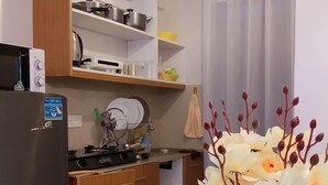 A compact kitchen with a refrigerator, stove, and wooden cabinets. There is a vase with flowers on the floor. - Stay.Plus Royal Suburbs By Tsavo (Nairobi)