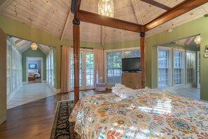 A bedroom with a four-poster bed, a television, and a view of a balcony.