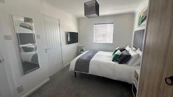 A bedroom with a bed, a TV, a window, and a door.