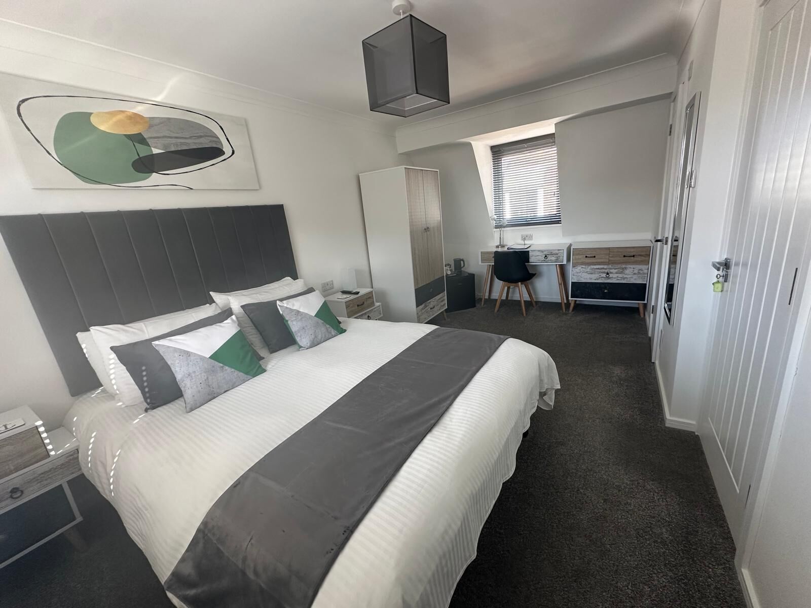 Une chambre d’hôtel avec un grand lit, un bureau, une chaise et une armoire.
