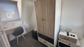 A bedroom with a desk, chair, wardrobe, bedside table, and a window with blinds. - Anchorage (Poole)