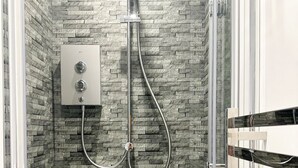 A shower with a stone wall, a control panel, and a glass door. - Anchorage (Poole)