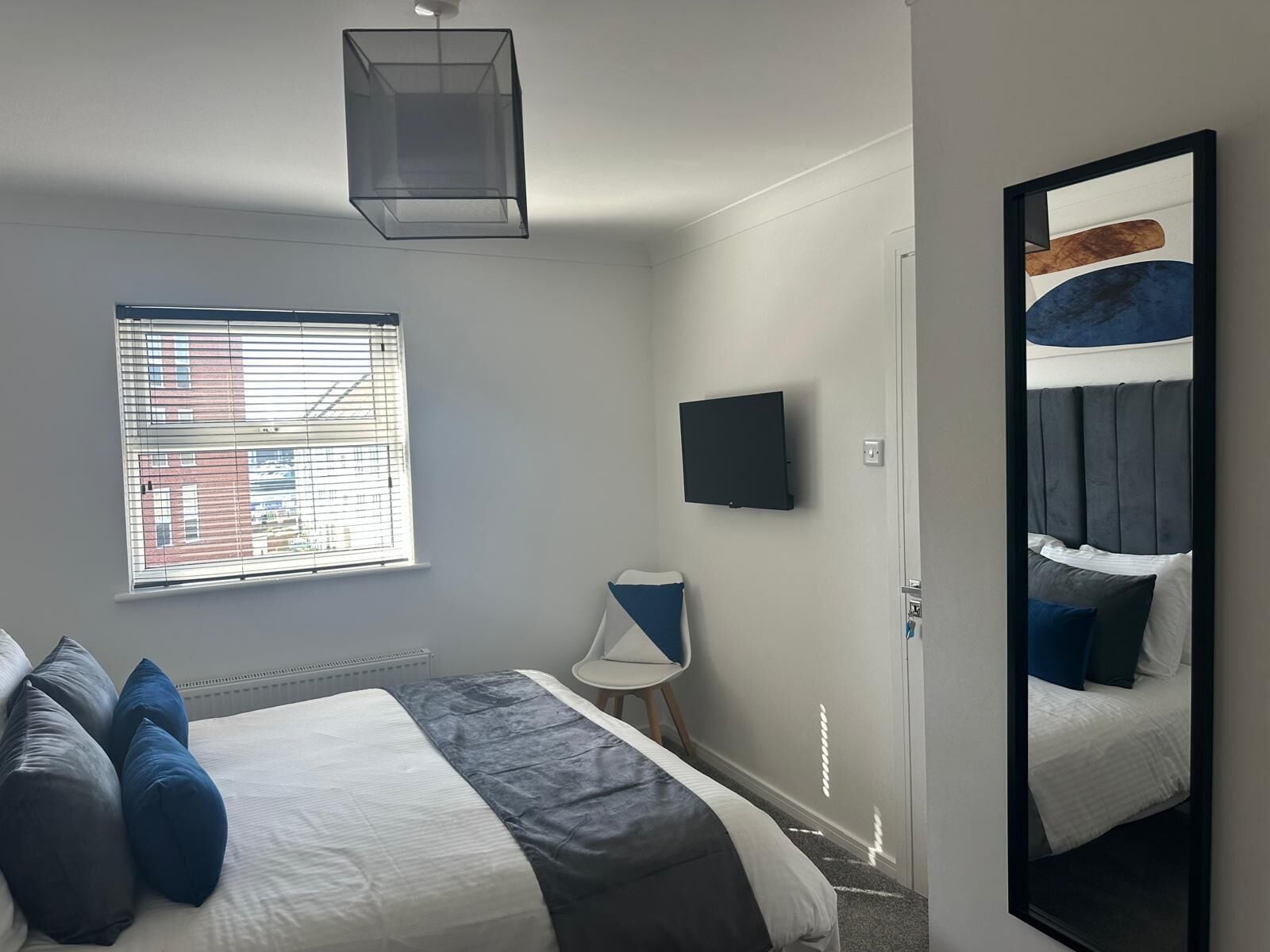 A bedroom with a bed, a TV, a window, and a mirror.