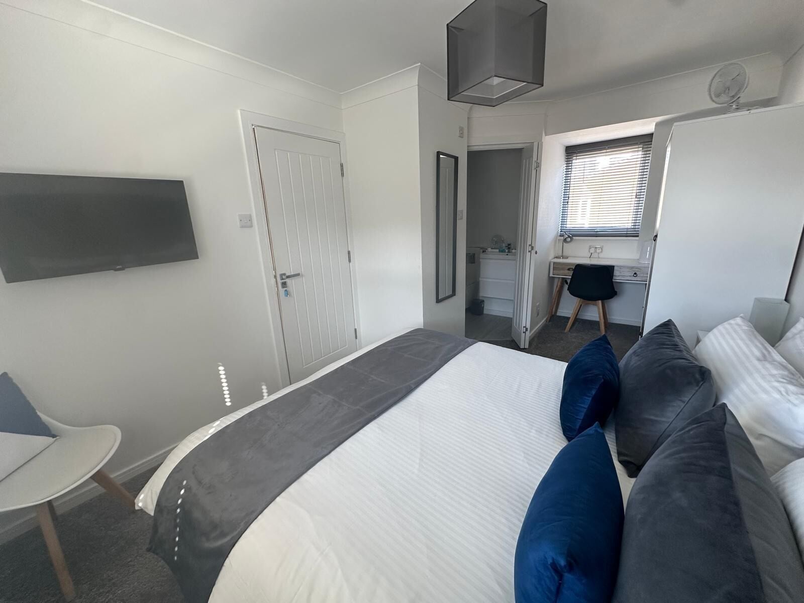 Un dormitorio con cama, escritorio, silla, televisor y puerta.