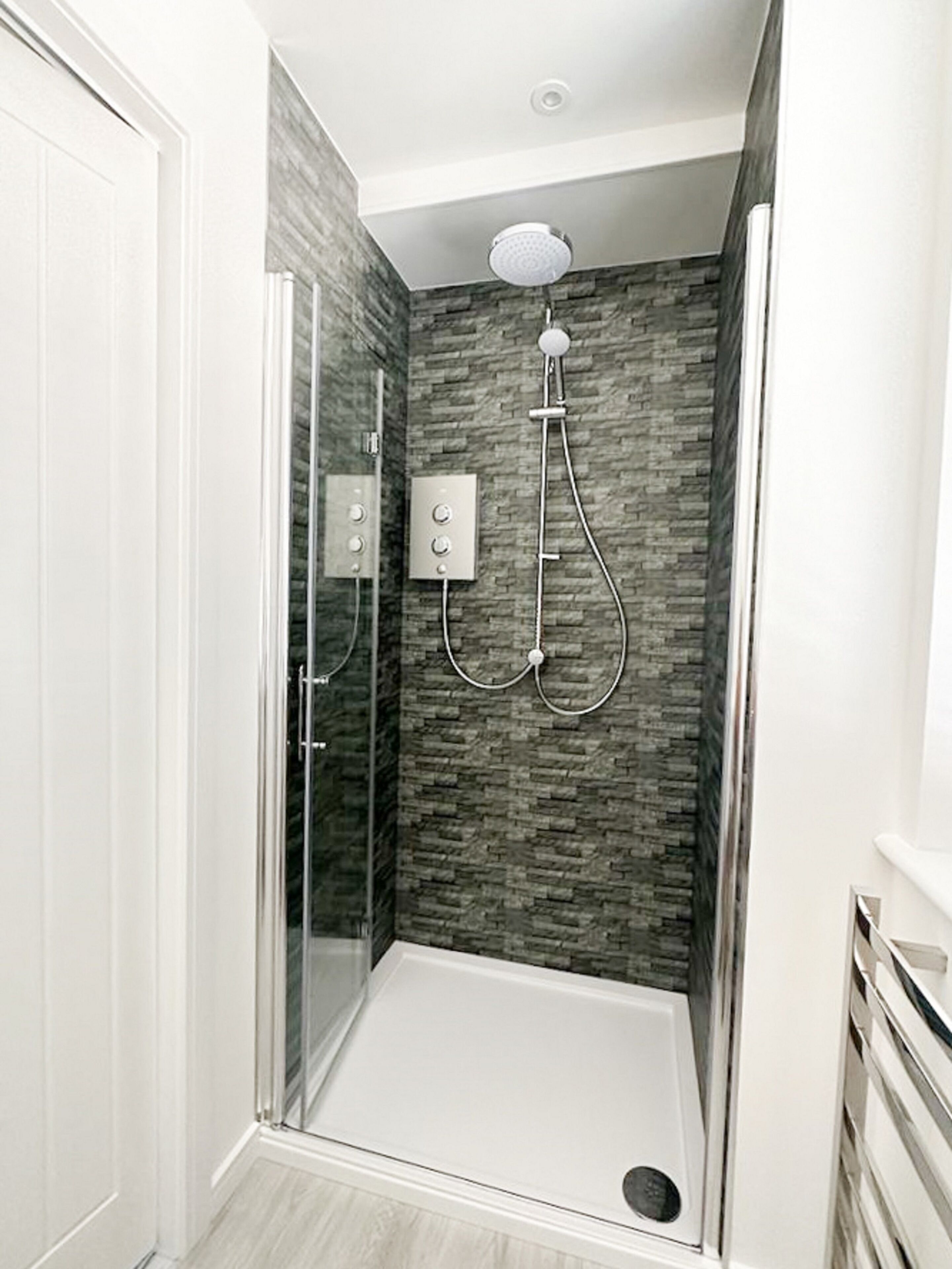 A walk-in shower with a glass door, a stone-textured wall, and a ceiling-mounted showerhead.