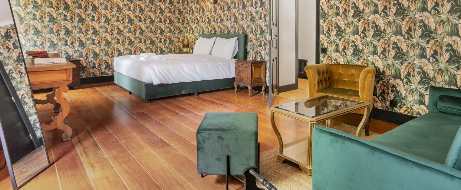 Ein Schlafzimmer mit einem Bett, einem grünen Sessel, einem kleinen Tisch und einem Nachttisch aus Holz.
