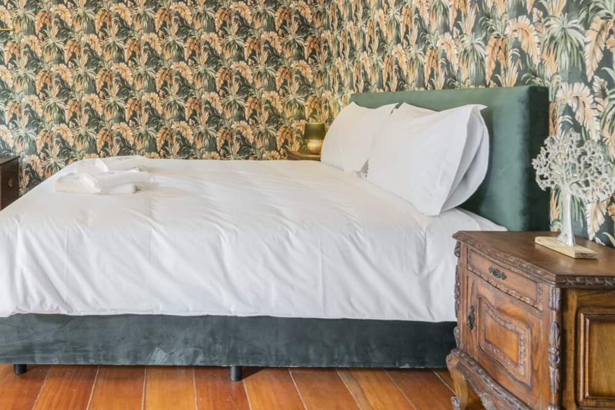 Quarto com uma cama grande, piso de madeira e papel de parede floral.