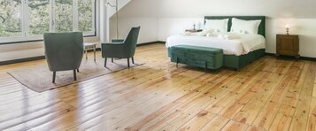 Un dormitorio con suelo de madera, una cama verde, una silla y una mesita de noche.