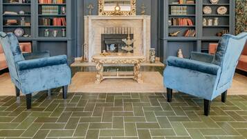 Un salón con dos sillones azules, una chimenea y estanterías llenas de libros y objetos decorativos.