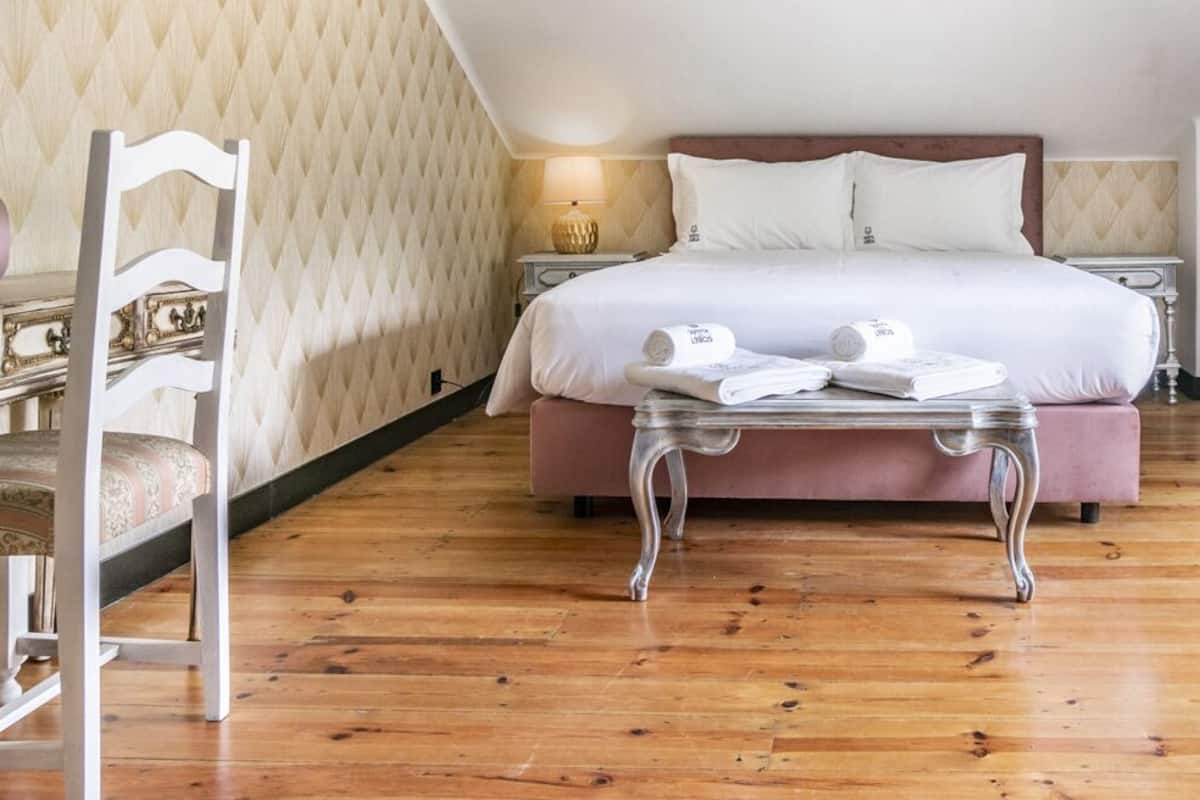 Quarto de hotel com cama, mesa de cabeceira, luminária, cômoda e uma cadeira.