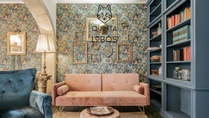 A cozy living room with a vintage sofa, a blue armchair, a bookshelf, and a decorative wall with framed pictures and a cat silhouette. - Quinta dos Lobos Boutique Hotel - Nature Experience (Sintra)