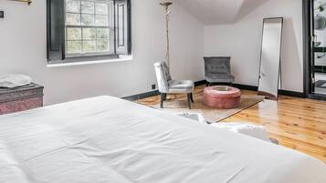 Ein Schlafzimmer mit einem großen Bett, einem Sessel, einem kleinen Hocker, einer Kommode und einem Spiegel.